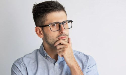 Portrait of pensive young businessman wearing eyeglasses. Caucasian man with hand on chin. Planning concept